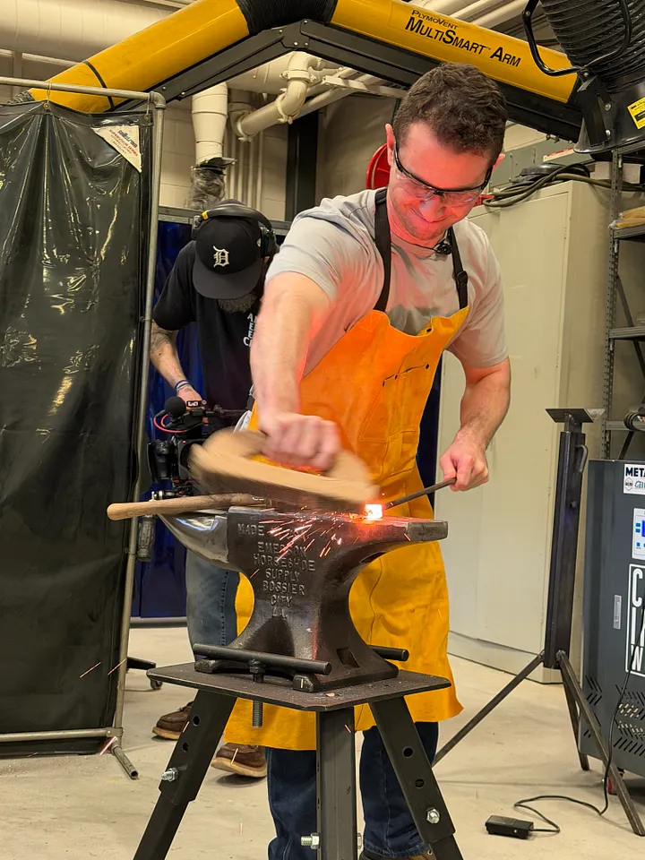 A man in a leather apron striking hot metal on an anvil