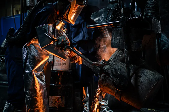 A worker in a heat suit tipping a crucible of molten metal