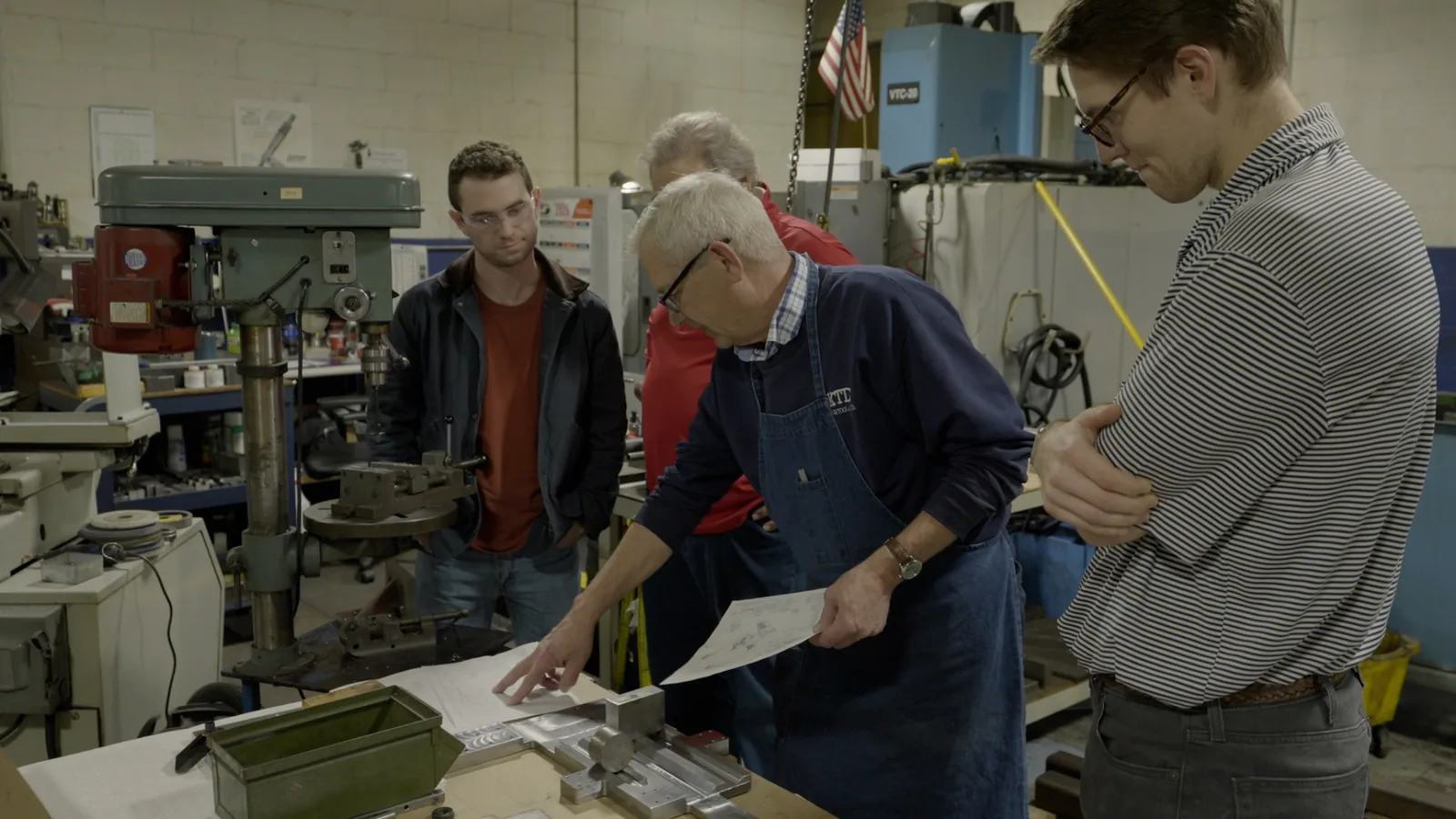 A toolmaker pointing at a drawing while explaining his craft to onlookers
